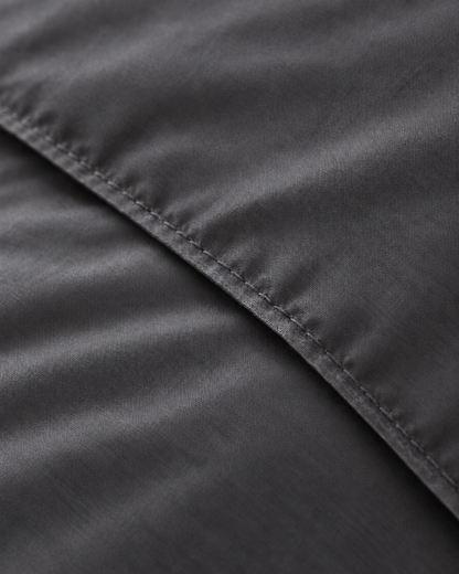 Macro of the stitched hem on a Charcoal Grey silky cotton duvet cover, showing the grey sateen weave and sheen.
