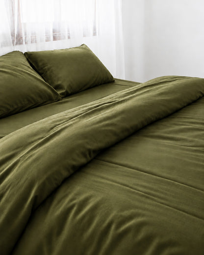 Juniper Green silky cotton duvet cover with one corner turned back on a bed by a white sheer curtain