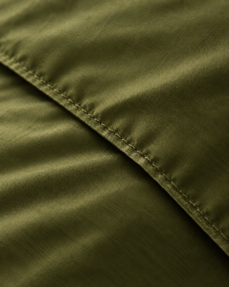 Macro of the stitched hem on a Juniper Green silky cotton duvet cover, showing the sateen sheen.