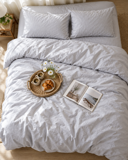 Silver Silky Cotton duvet cover from above with a rattan tray of coffee and croissants and a magazine
