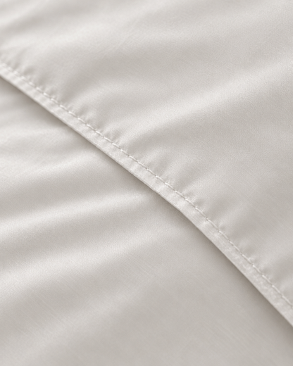 Macro of the stitched hem on a Milky White silky cotton duvet cover, showing the white sateen weave and sheen.