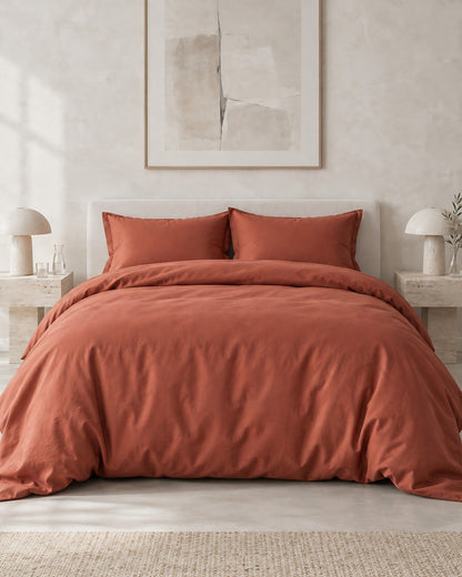 Rust silky cotton duvet cover against a limewashed plaster wall between travertine bedside tables