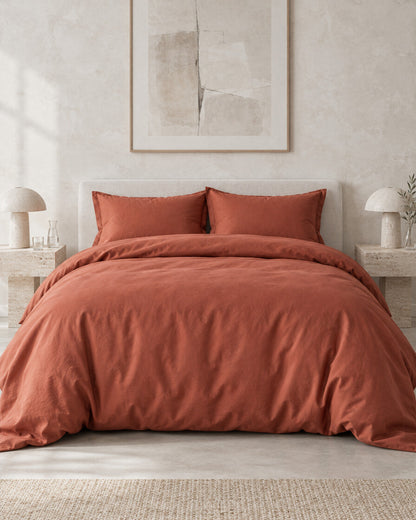 Terracotta silky cotton duvet cover against a limewashed plaster wall between travertine bedside tables