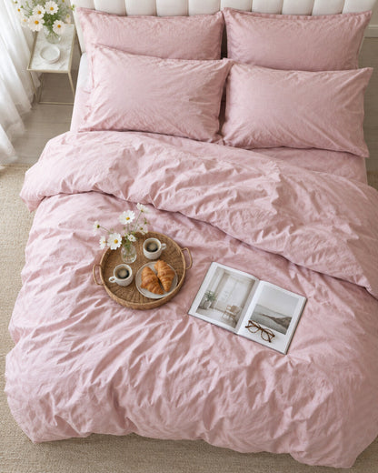 Blush pink silky cotton duvet cover seen from above with a breakfast tray of coffee and croissants