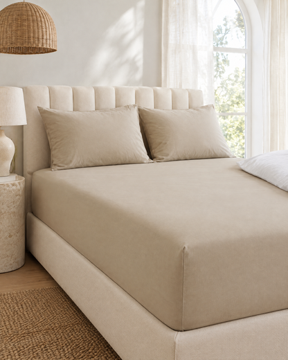 Beige plain cotton percale fitted sheet on a made bed in a bright bedroom