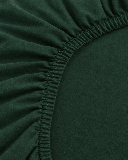 Close-up of the elasticated corner of a Forest Green plain cotton fitted sheet in bottle green