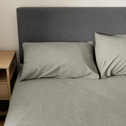 Mint Grey plain cotton fitted sheet and pillowcases on a made bed with a charcoal headboard