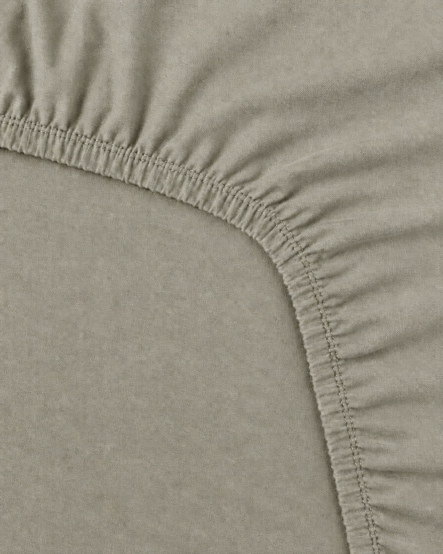 Close-up of the elasticated corner and stitched edge of a Mint Grey plain cotton fitted sheet