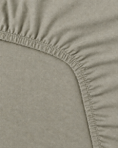 Close-up of the elasticated corner and stitched edge of a Mint Grey plain cotton fitted sheet
