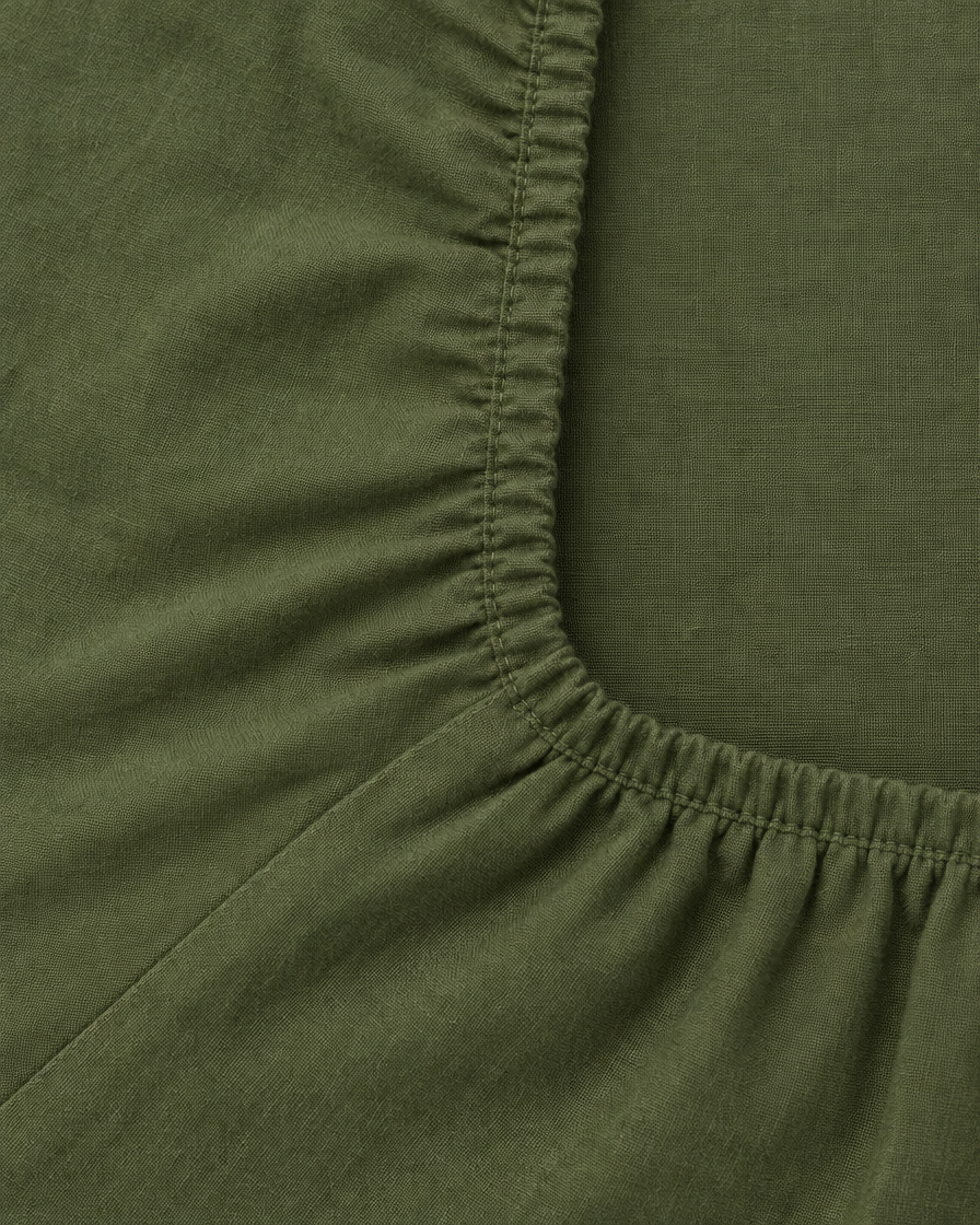Close-up of elasticated corner and stitched edge of the fitted sheet in Olive Plain Cotton