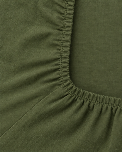 Close-up of elasticated corner and stitched edge of the fitted sheet in Olive Plain Cotton