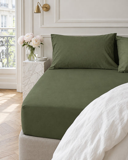 Olive green plain cotton fitted sheet in a Parisian bedroom with panelled walls and fresh peonies