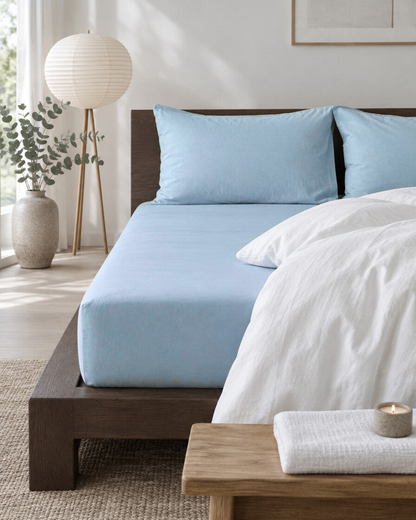 Baby blue plain cotton fitted sheet and pillowcases on a low dark wood bed in a calm Japandi bedroom