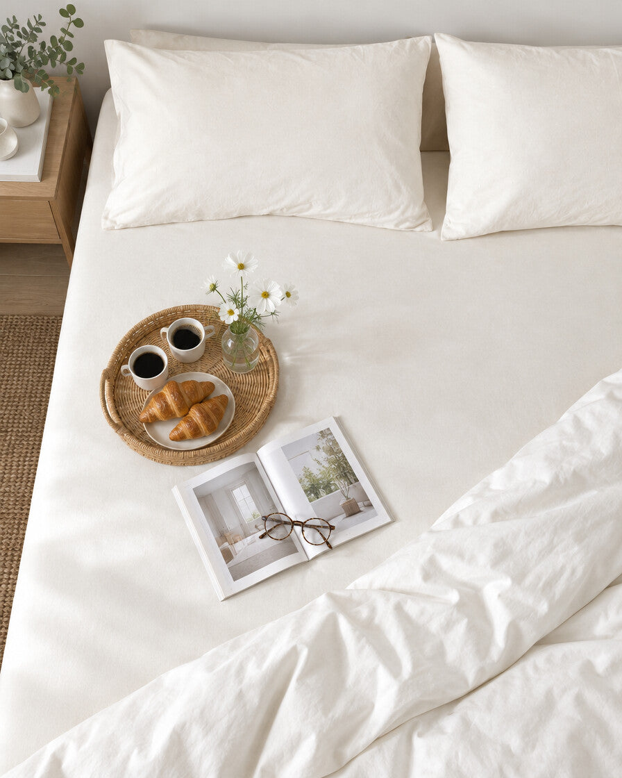 White plain cotton fitted sheet seen from above with a breakfast tray of coffee and croissants