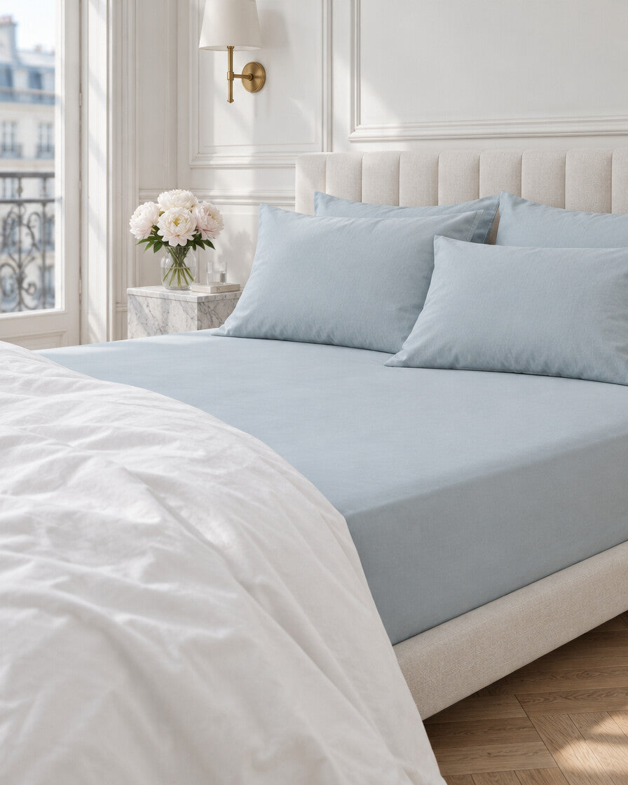 Pale blue plain cotton fitted sheet in a Parisian bedroom with panelled walls and fresh peonies