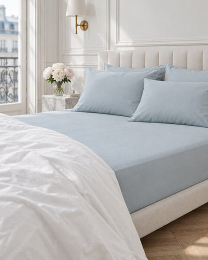 Pale blue plain cotton fitted sheet in a Parisian bedroom with panelled walls and fresh peonies