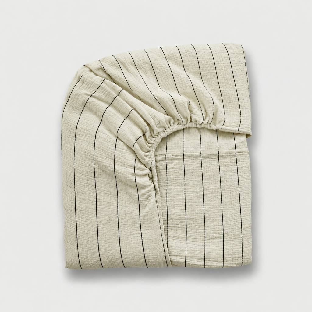 Folded cloud cotton fitted sheet with Black Pinstripe on off-white crinkled muslin, elastic corner visible.