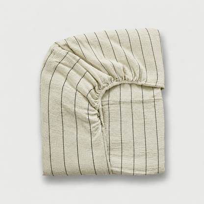 Folded cloud cotton fitted sheet with Black Pinstripe on off-white crinkled muslin, elastic corner visible.