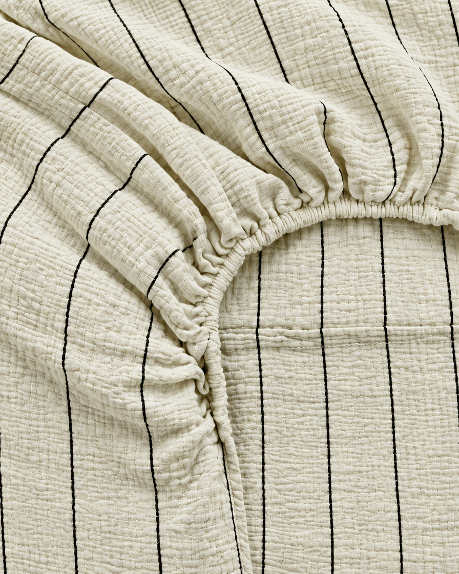 Close-up of elasticated corner and stitched edge of the fitted sheet in Black Pinstripe Cloud Cotton