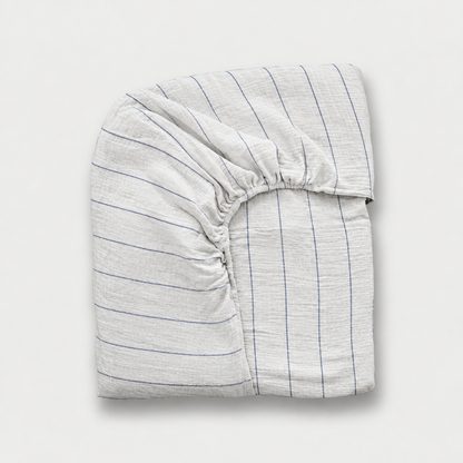 Folded cloud cotton fitted sheet with fine Blue Pinstripe on off-white crinkled muslin, plain background.