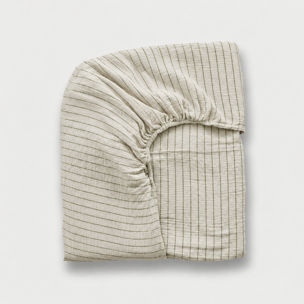 Folded cloud cotton fitted sheet in off-white muslin with fine Green Pinstripe and an elasticated corner.