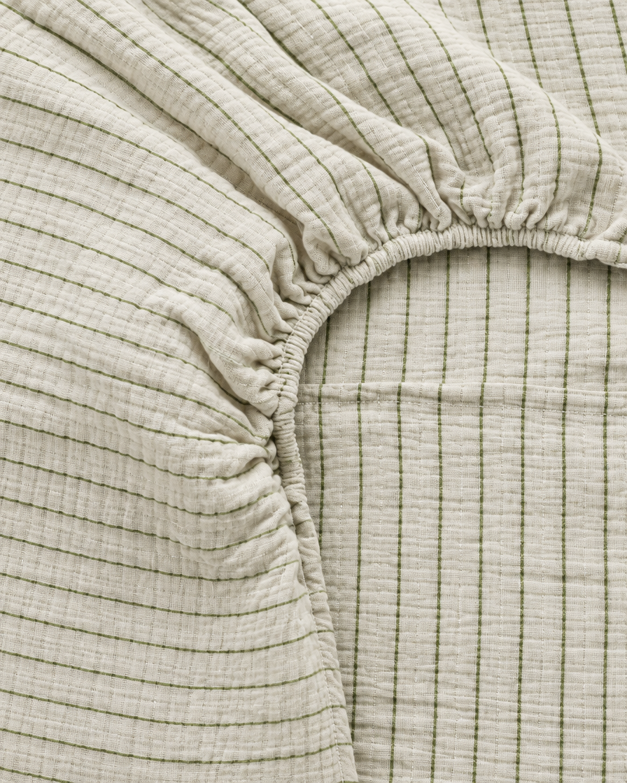 Close-up of elasticated corner and stitched edge of the fitted sheet in Green Pinstripe Cloud Cotton