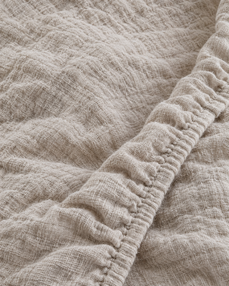 Close-up of elasticated corner and stitched edge of the fitted sheet in Oat Milk Cloud Cotton