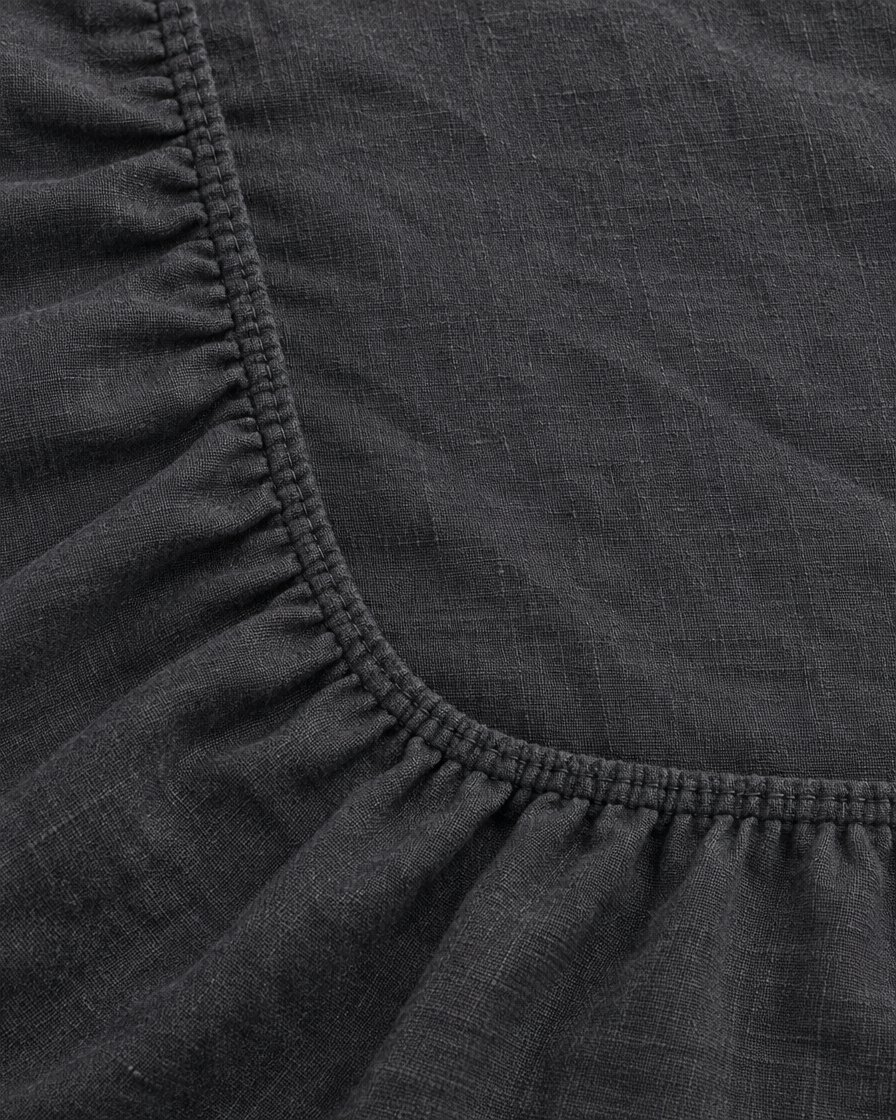 Close-up of elasticated corner and stitched edge of the fitted sheet in Charcoal Linen