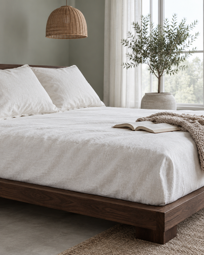 White French linen fitted sheet on a walnut platform bed with a knit throw and an open book
