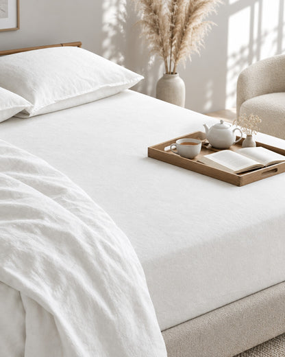 White French linen fitted sheet with a tea tray and open book, a boucle armchair in the corner