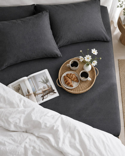 Charcoal French linen fitted sheet seen from above with a breakfast tray of coffee and croissants