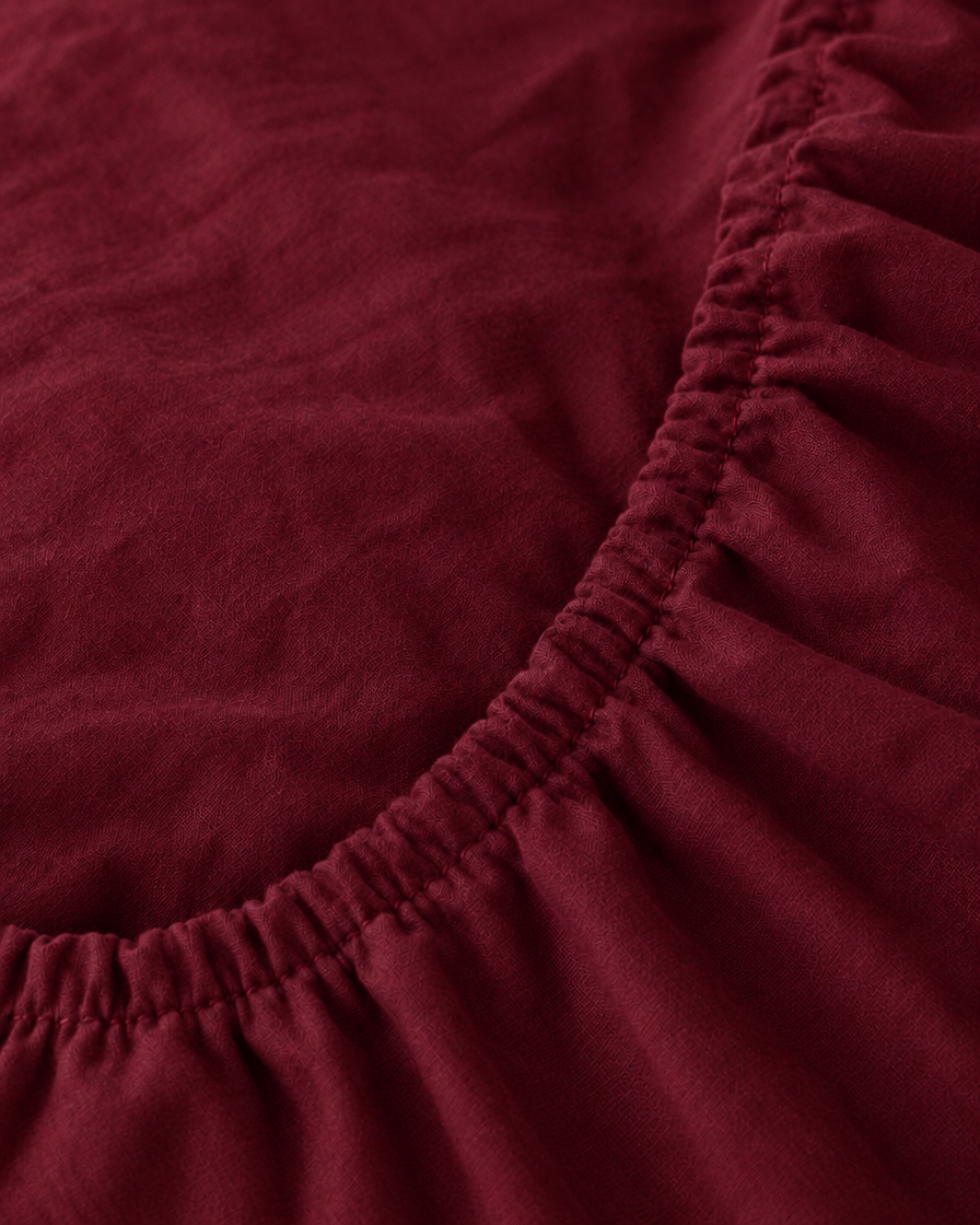 Macro of the gathered elastic corner of a Burgundy Red plain cotton fitted sheet.
