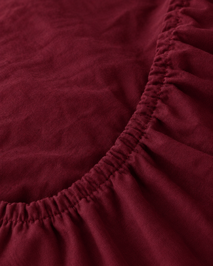Macro of the gathered elastic corner of a Burgundy Red plain cotton fitted sheet.