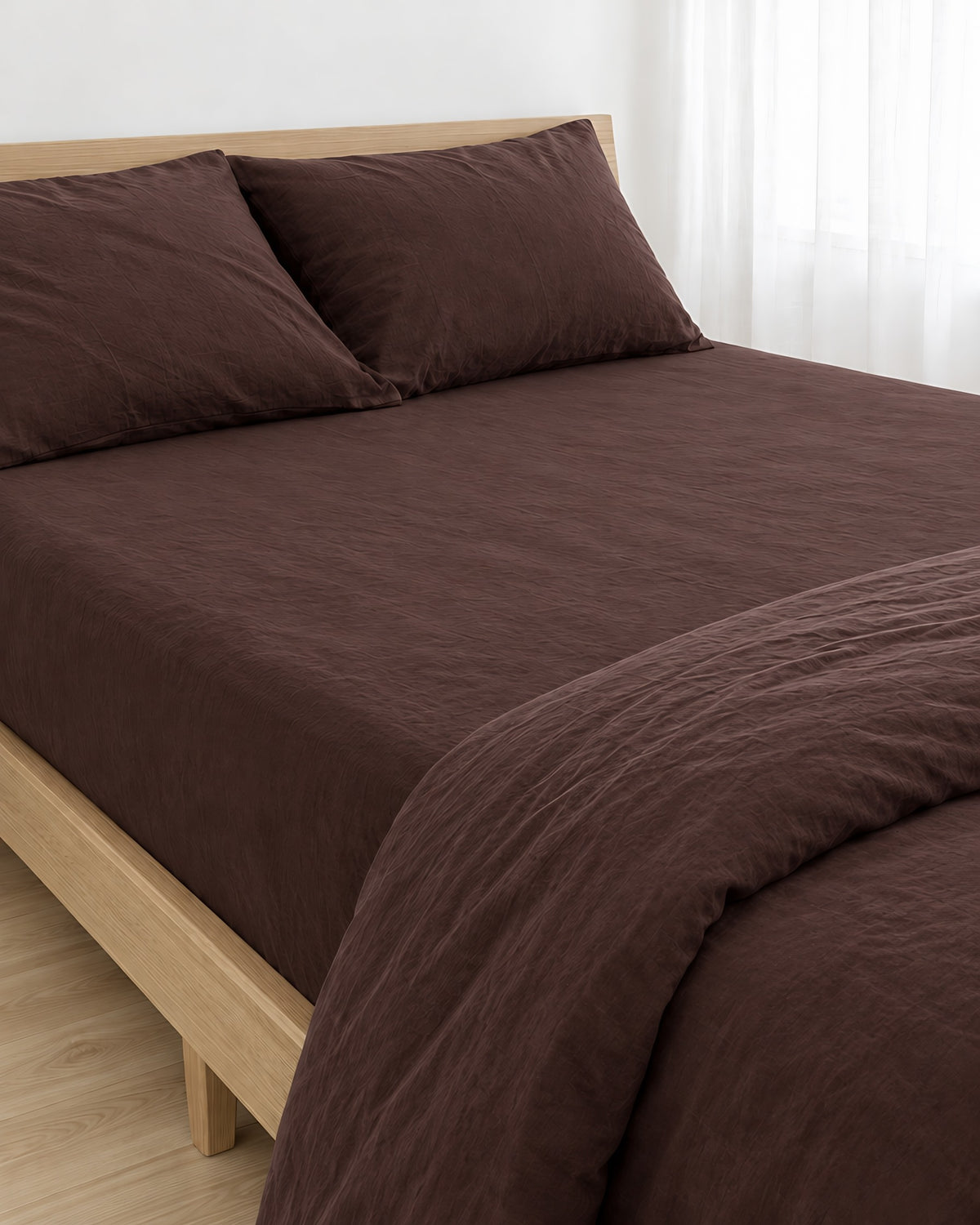 Chocolate plain cotton fitted sheet pulled taut over a mattress on an oak bed with matching pillows