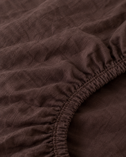 Macro of the gathered elastic corner of a Chocolate plain cotton fitted sheet.