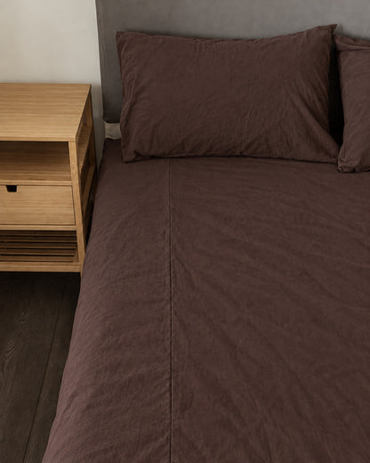 Chocolate plain cotton fitted sheet and pillow on a bed beside an oak bedside table
