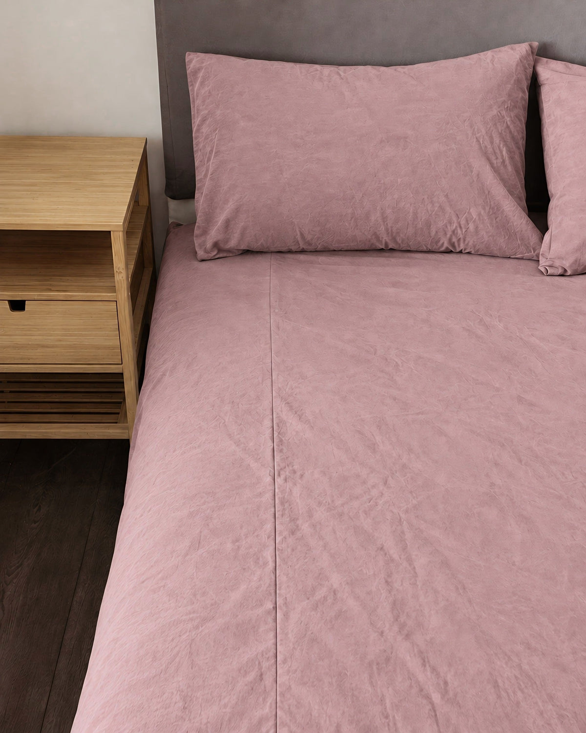 Dust Pink plain cotton fitted sheet and pillow on a bed beside an oak bedside table