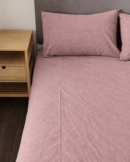 Dust Pink plain cotton fitted sheet and pillow on a bed beside an oak bedside table