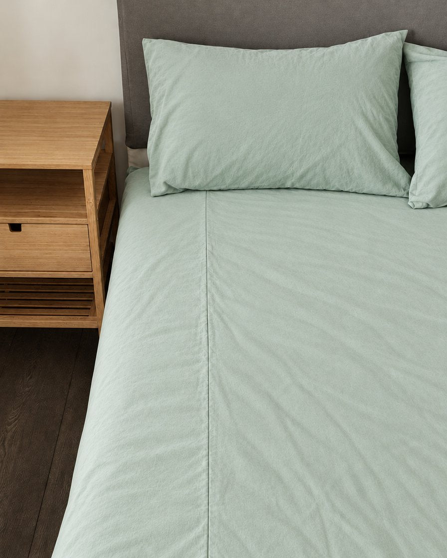 Mint Green plain cotton fitted sheet and pillows on a bed beside an oak bedside table