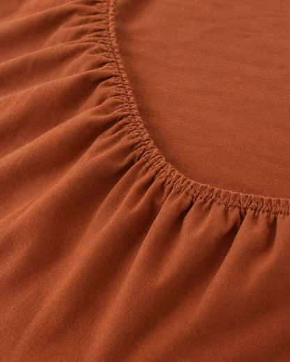 Macro of the gathered elastic corner of a Terracotta plain cotton fitted sheet.
