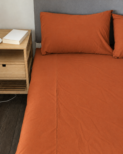 Terracotta plain cotton fitted sheet and pillow on a bed.