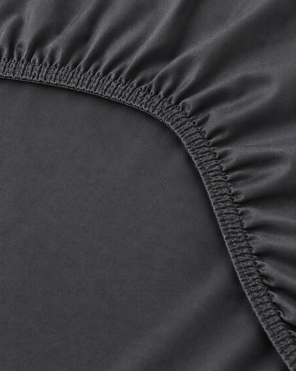 Close-up of elasticated corner and stitched edge of the fitted sheet in Charcoal Grey Silky Cotton