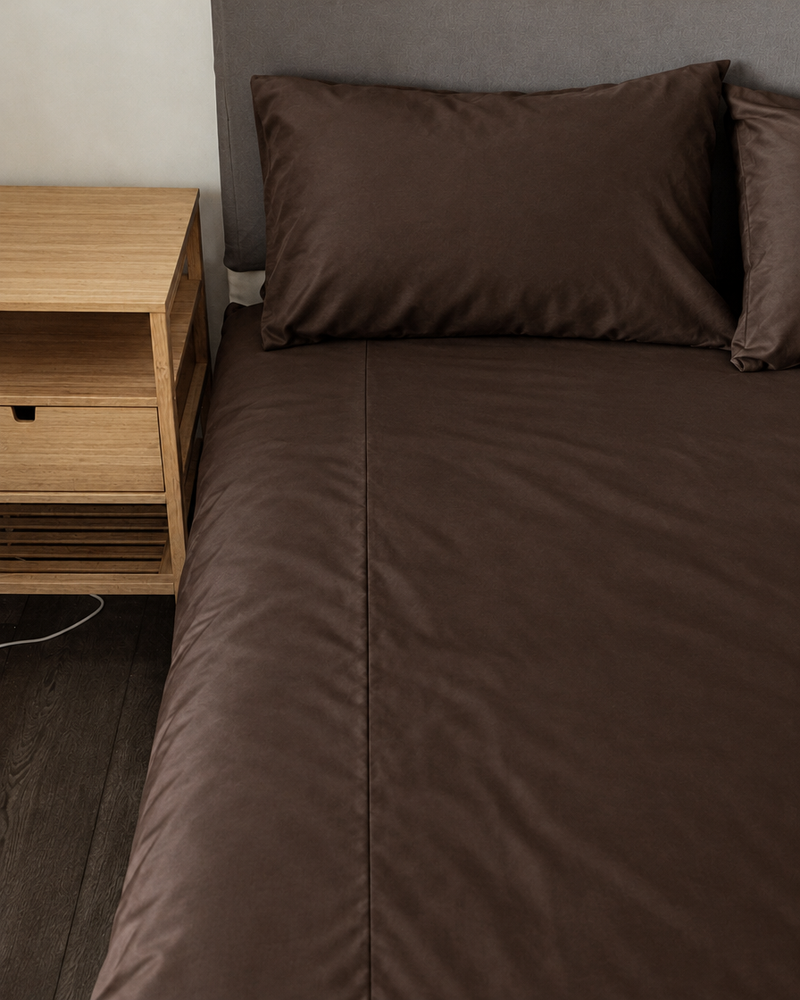 Chocolate silky cotton fitted sheet and pillow on a bed beside an oak bedside table.