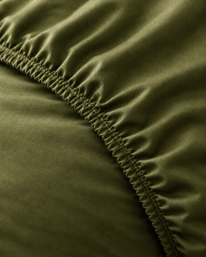 Macro of the gathered elastic corner of a Juniper Green silky cotton fitted sheet.