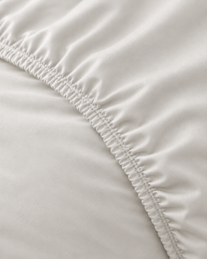 Macro of the gathered elastic corner of a Milky White silky cotton fitted sheet in white cotton sateen.