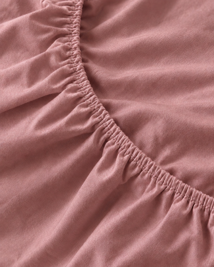 Macro of the gathered elastic corner of a Rose Pink silky cotton fitted sheet.