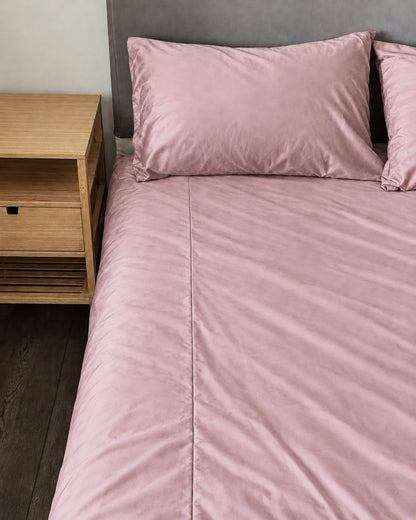 Rose Pink silky cotton fitted sheet and pillow on a bed beside an oak bedside table