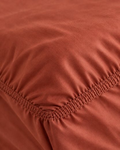 Macro of the gathered elastic corner of a Rust silky cotton fitted sheet.