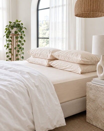 Cream and beige silky cotton fitted sheet beneath an arched window with a trailing pothos and rattan pendant