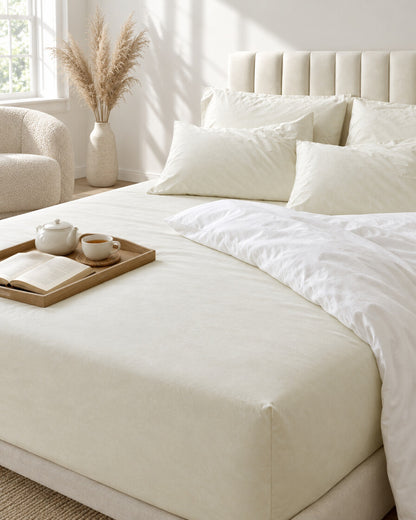 Cream silky cotton fitted sheet with a tea tray and open book, a boucle armchair in the corner
